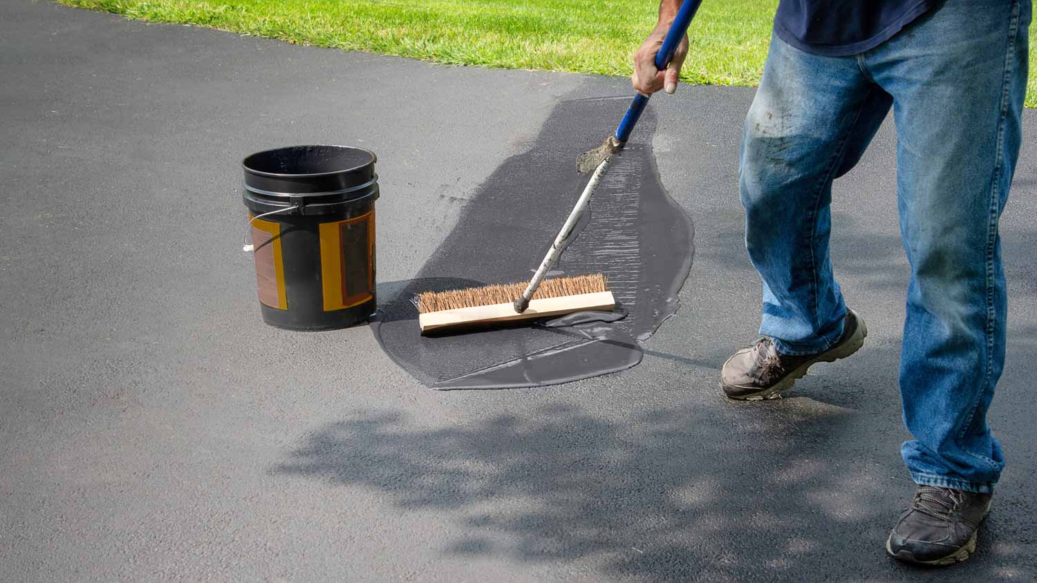 man applying asphalt sealant driveway   