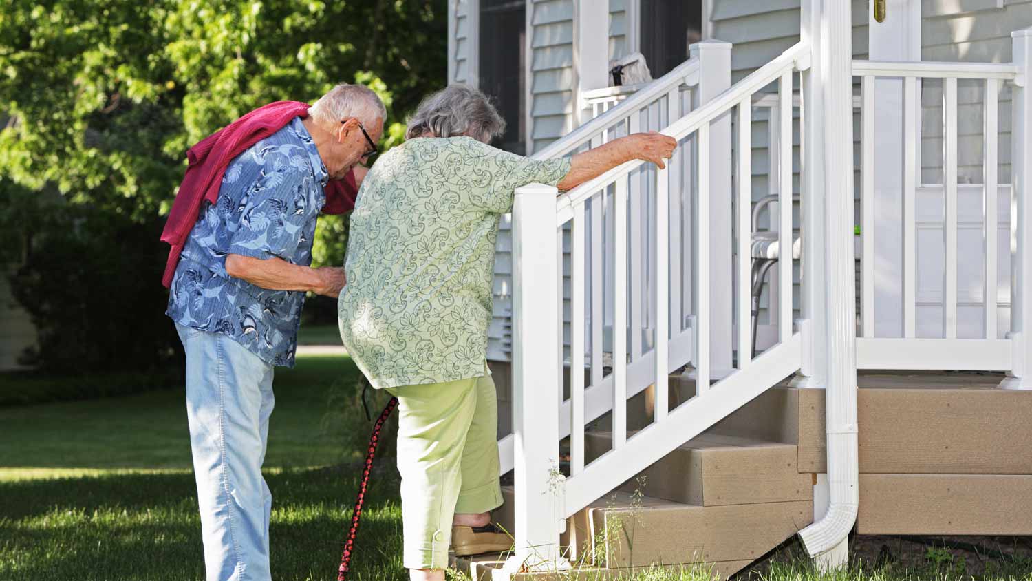 elderly couple using banister to climb porch steps