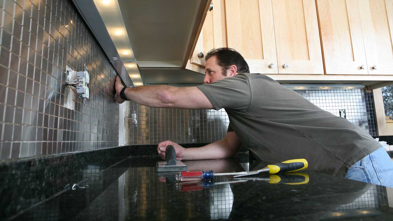 man installing metal backsplash in kitchen