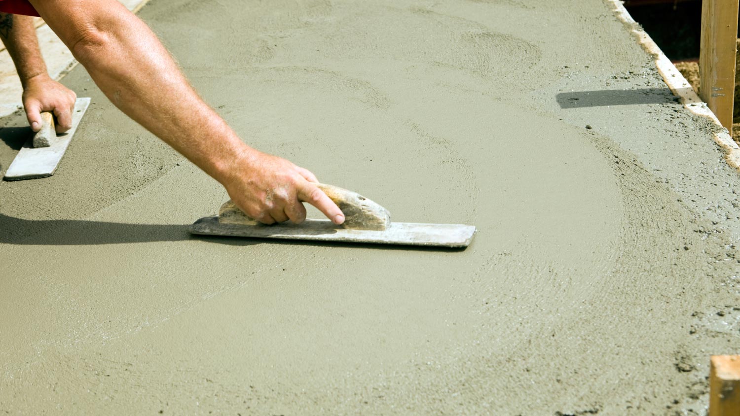 Worker using concrete trowel to smooth a fresh concrete slab