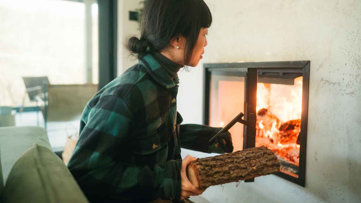 Woman adding firewood log to a fireplace 