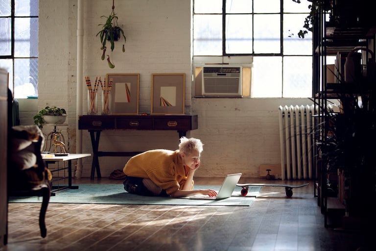 person lays on rug looking at laptop in loft style room with window air conditioner