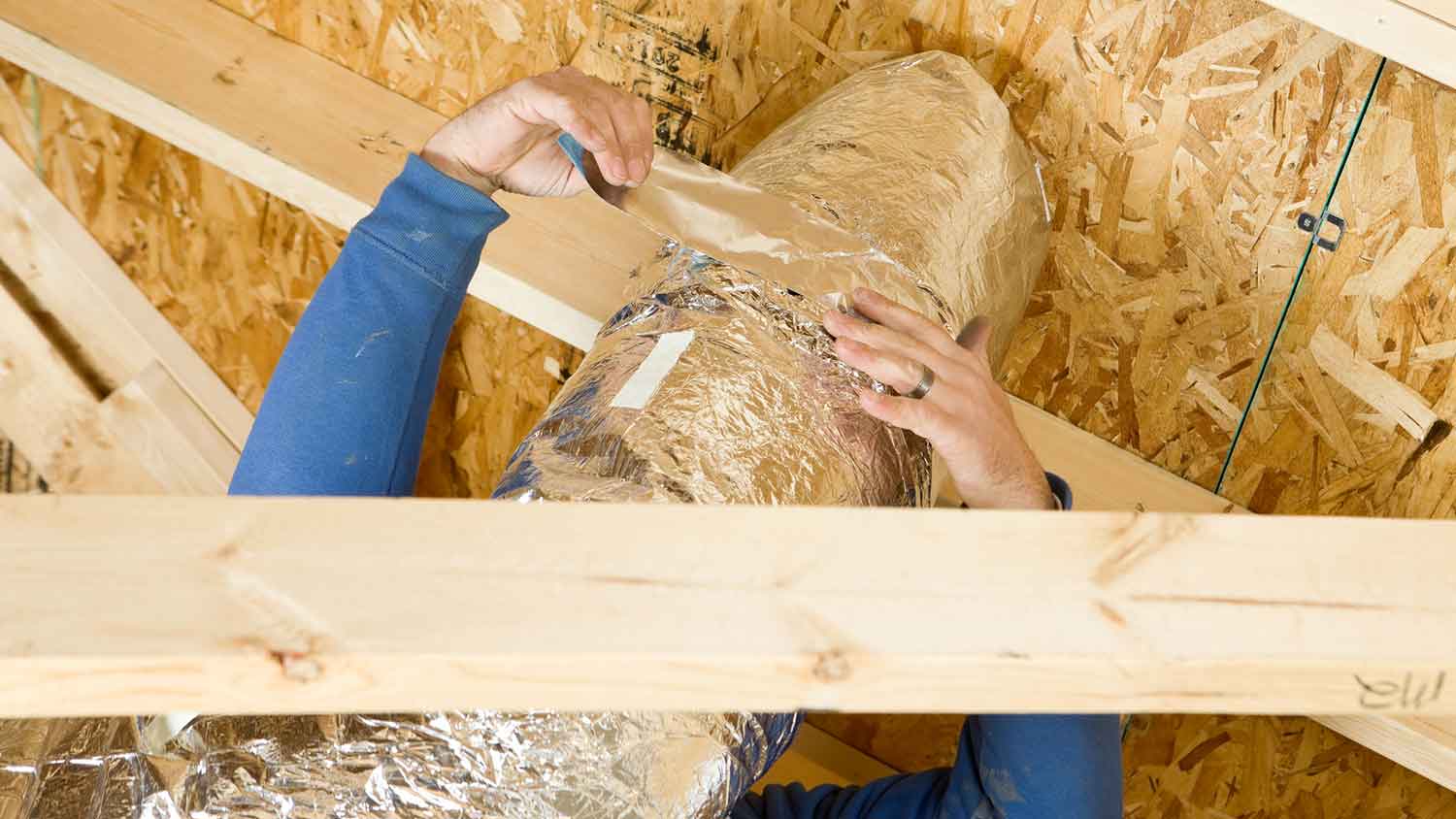 Worker insulating air duct in the attic 