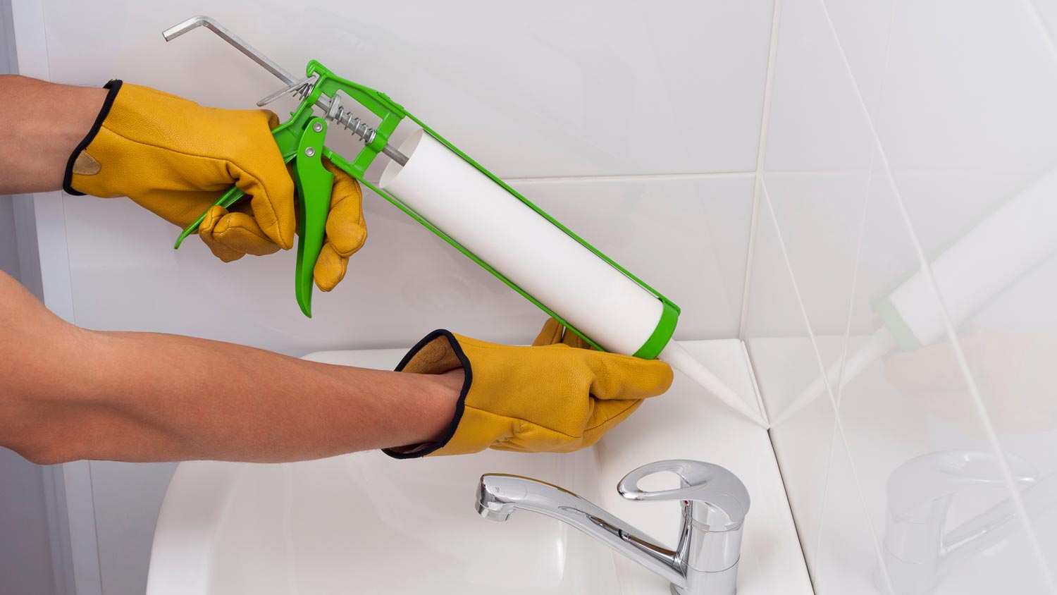 man applying caulk along sink and wall tiles