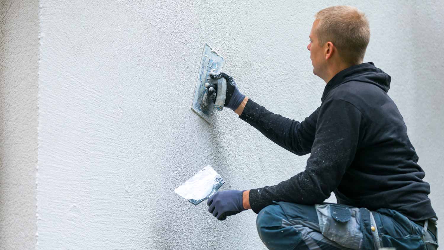 man applying stucco to home exterior