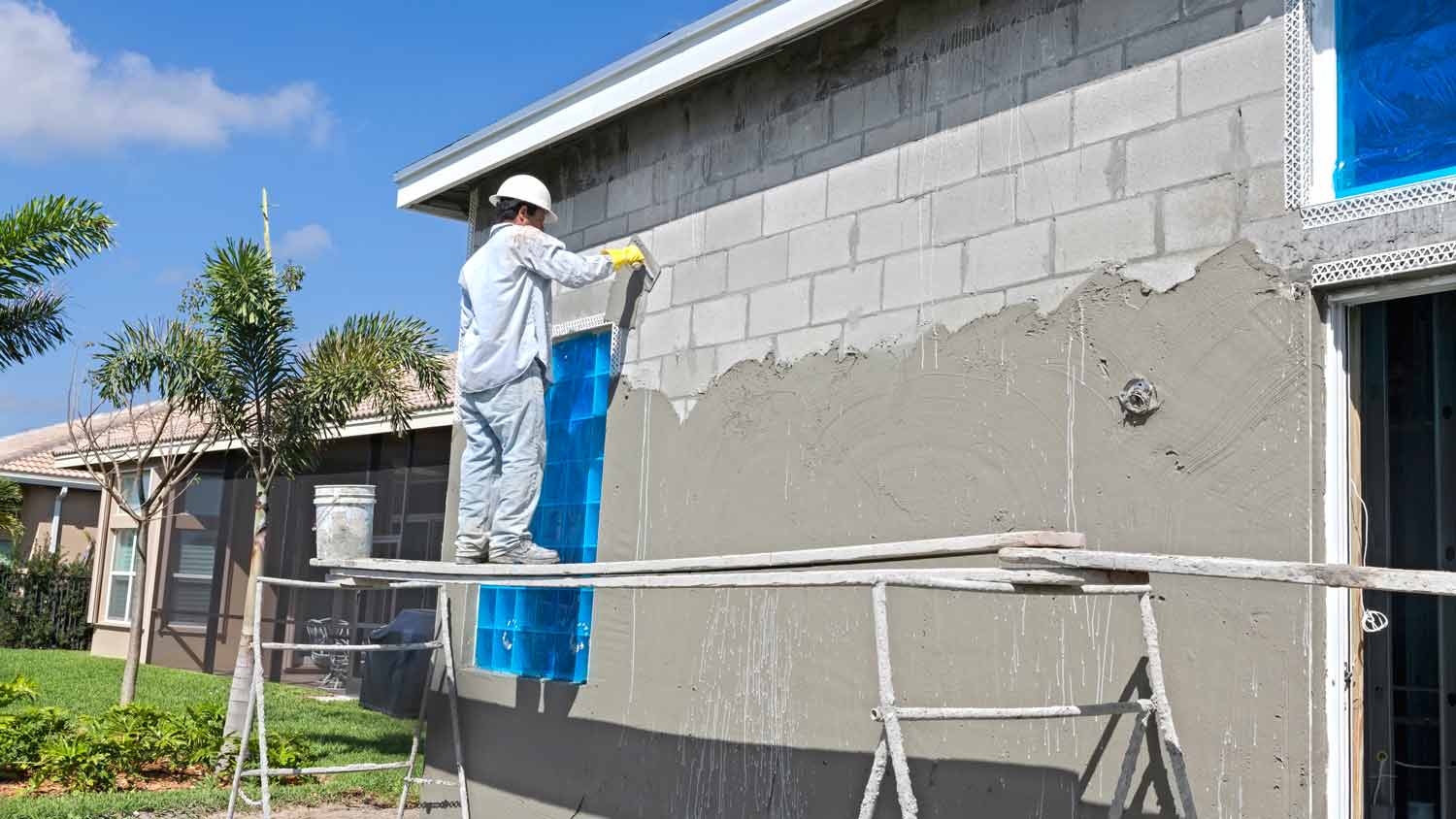 worker putting stucco over brick house