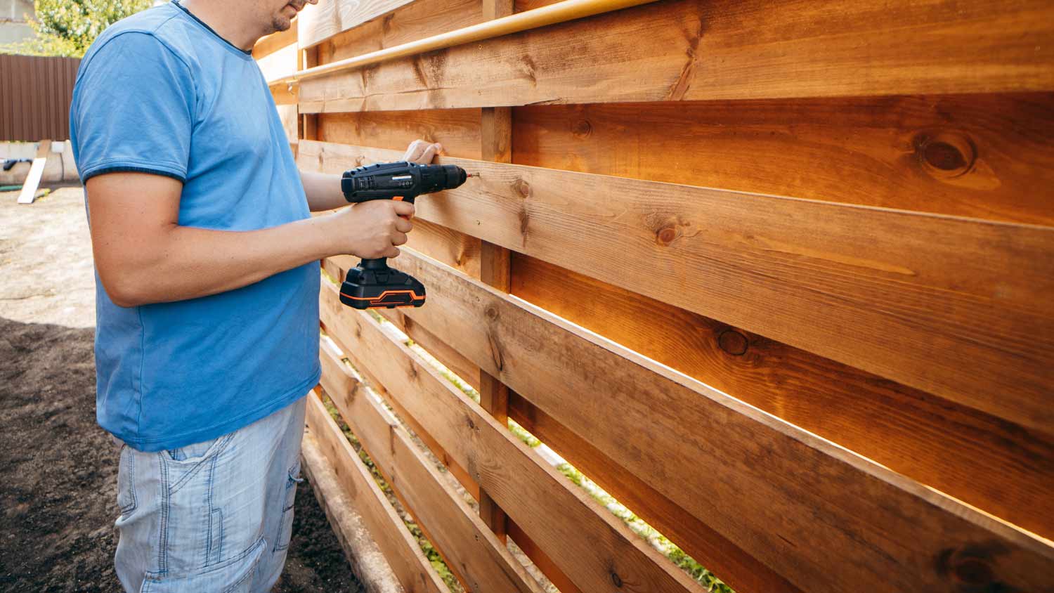 man reassembling wood fence with drill