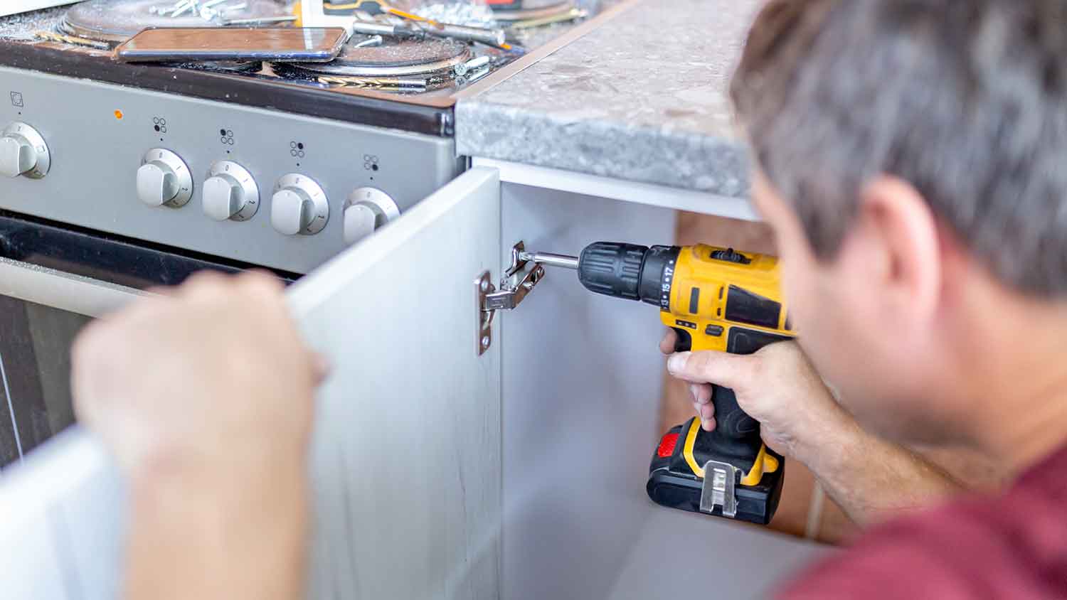 Man using electric screwdriver to adjust cabinet door