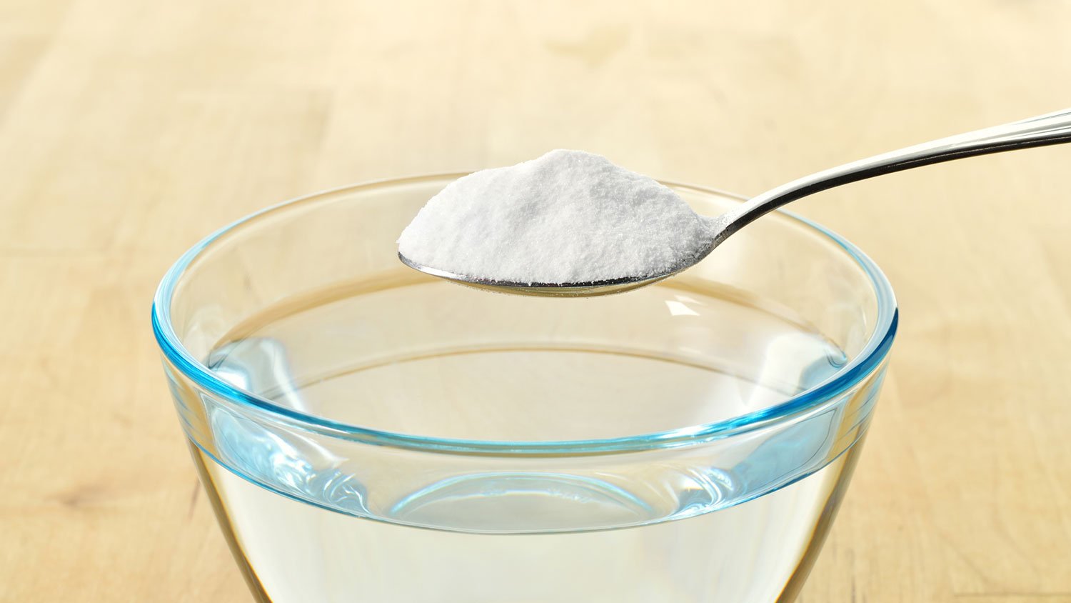 A spoon of baking soda over a bowl with water