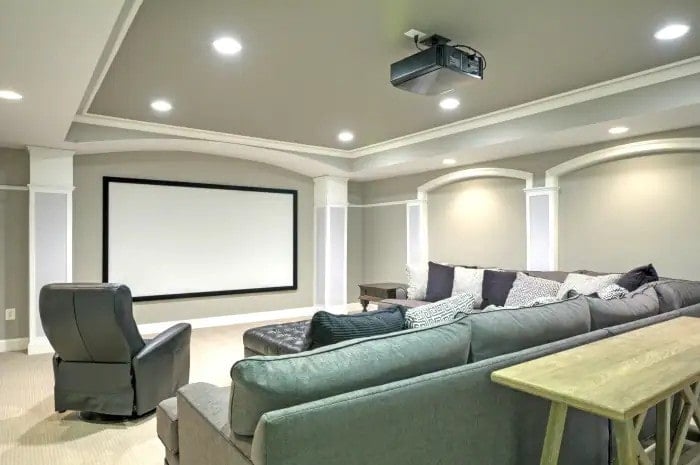 Basement theater area with couches, projector screen, and tray ceiling