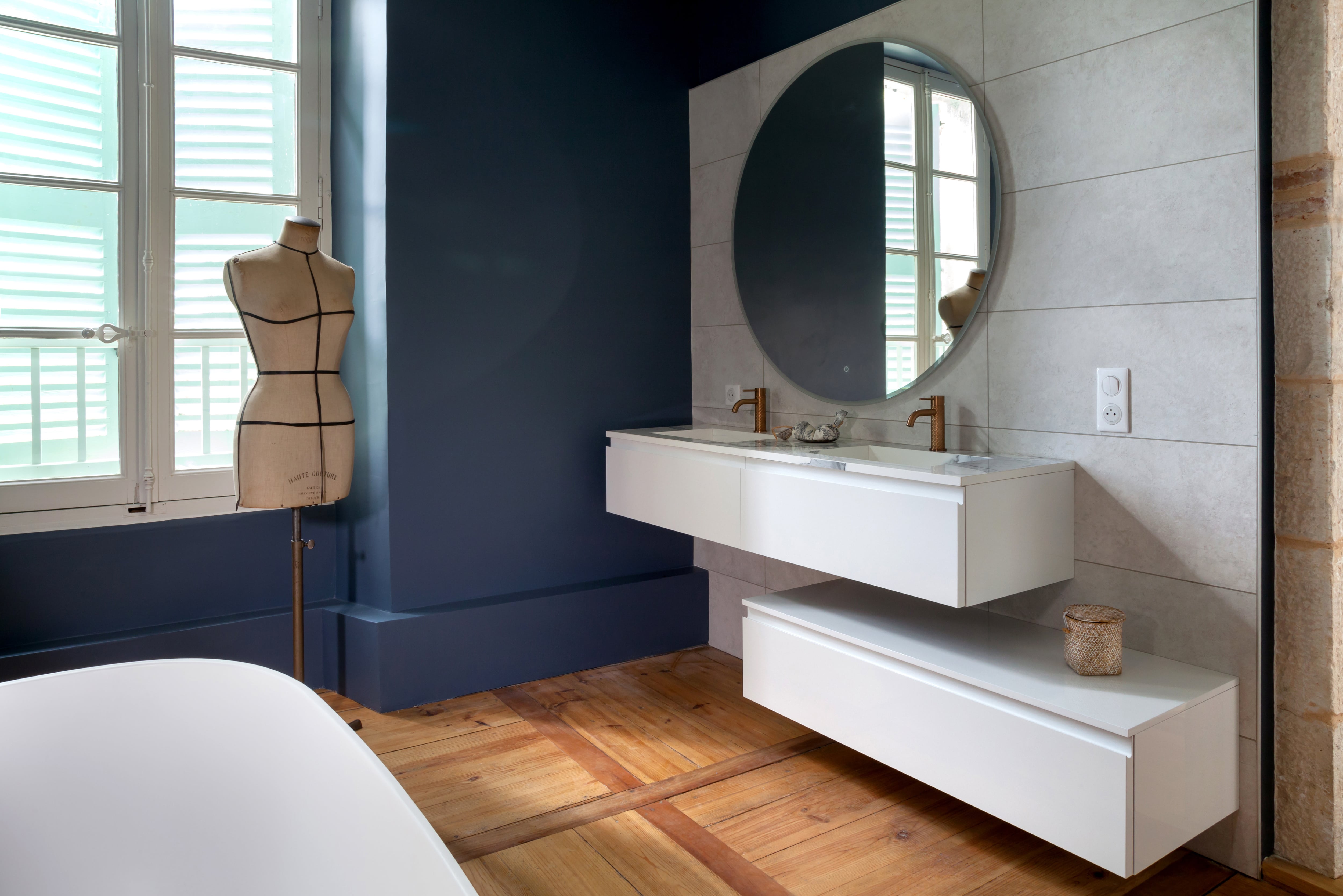 Large bathroom with wood floors, blue walls, white floating vanities, and whole-wall tile