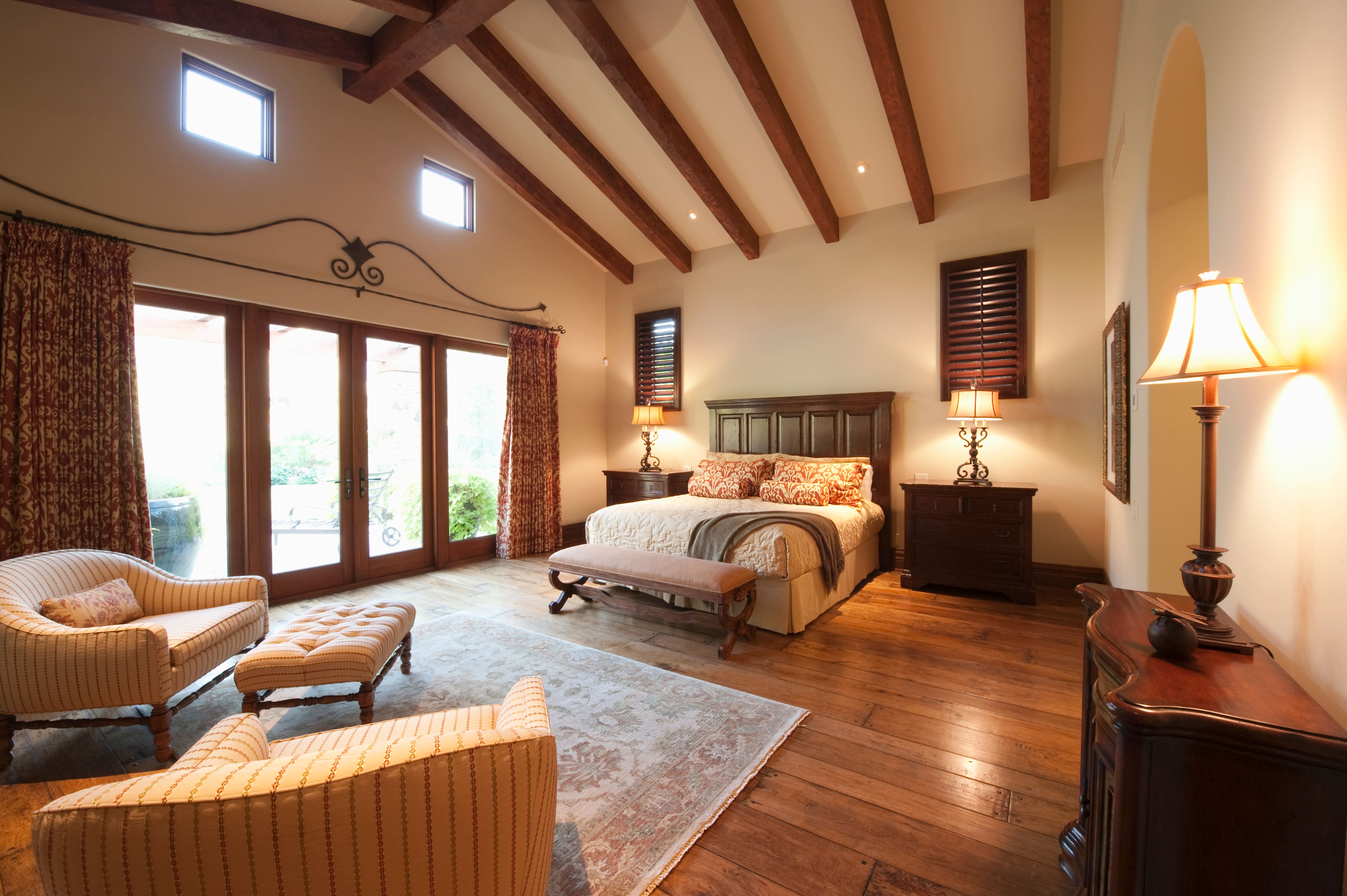 Spacious bedroom with wood floors, seating area, large bed, curtains, and ceiling beams