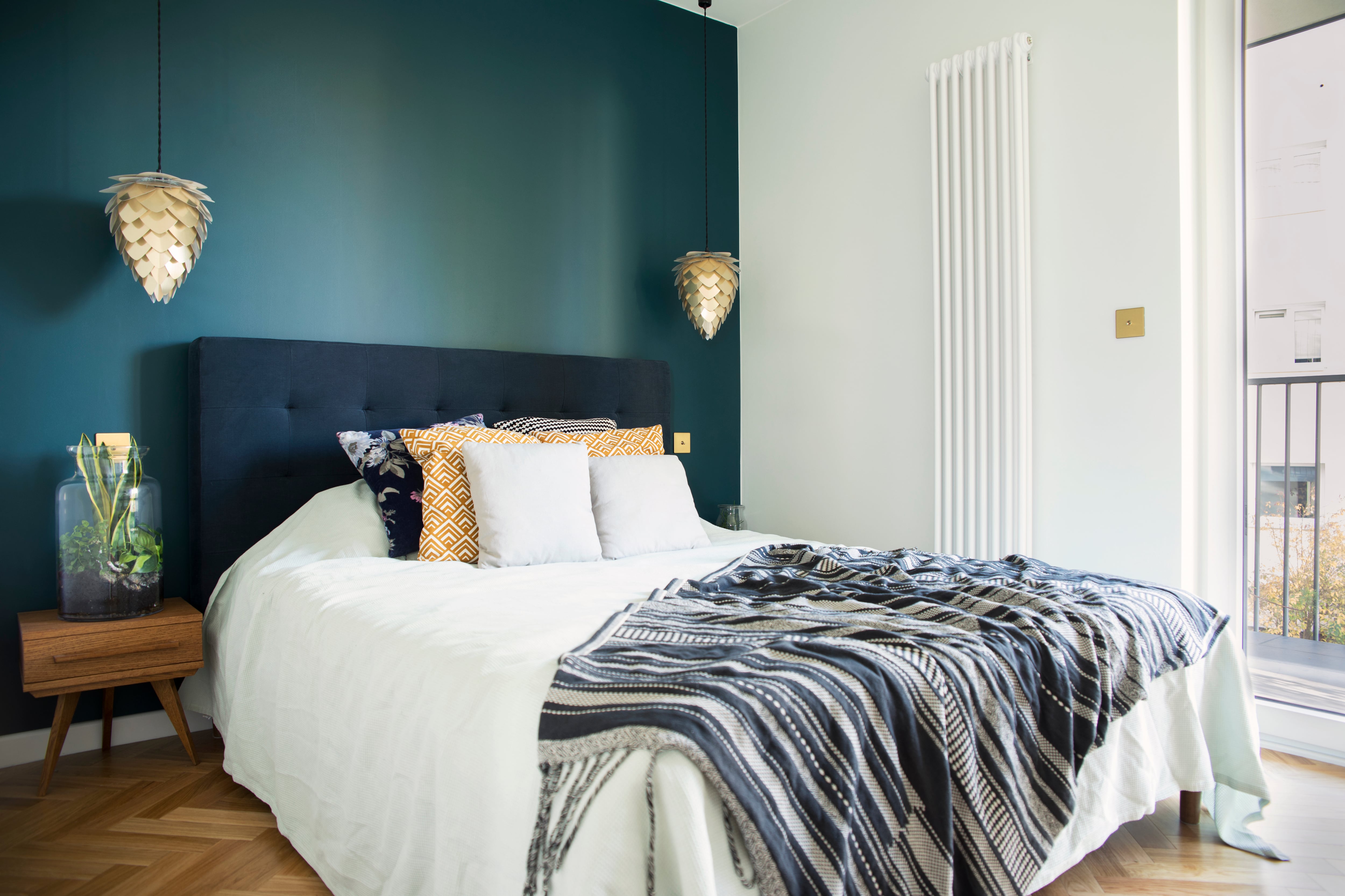 Elegant bedroom with a bed, green velvet cushioned headboard, green accent wall, and gold hanging lights