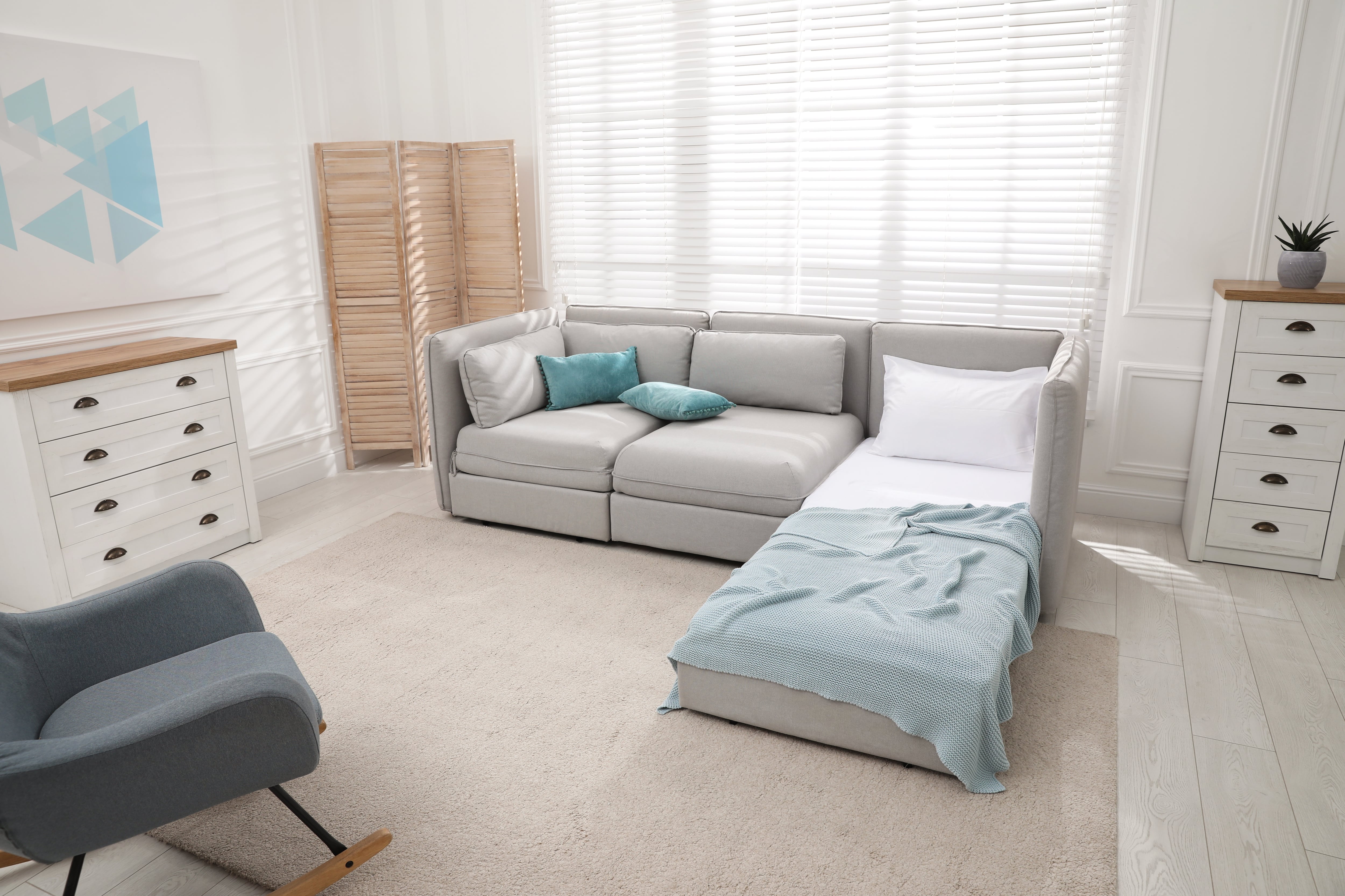 Bright guest bedroom with sleeper sofa, rocking chair, wooden room divider, and jute rug