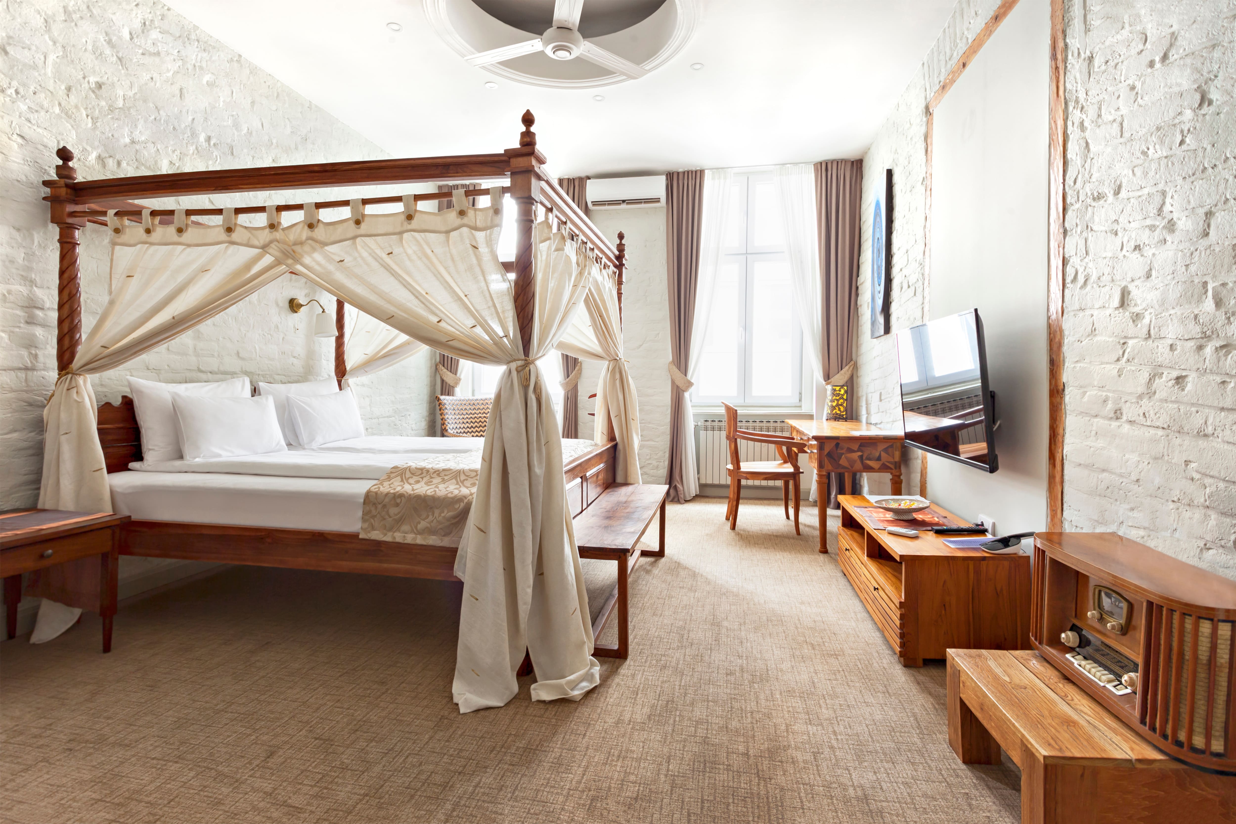Antique canopy bed in a modern bedroom with white brick walls, carpet floors, and mid-century modern furniture