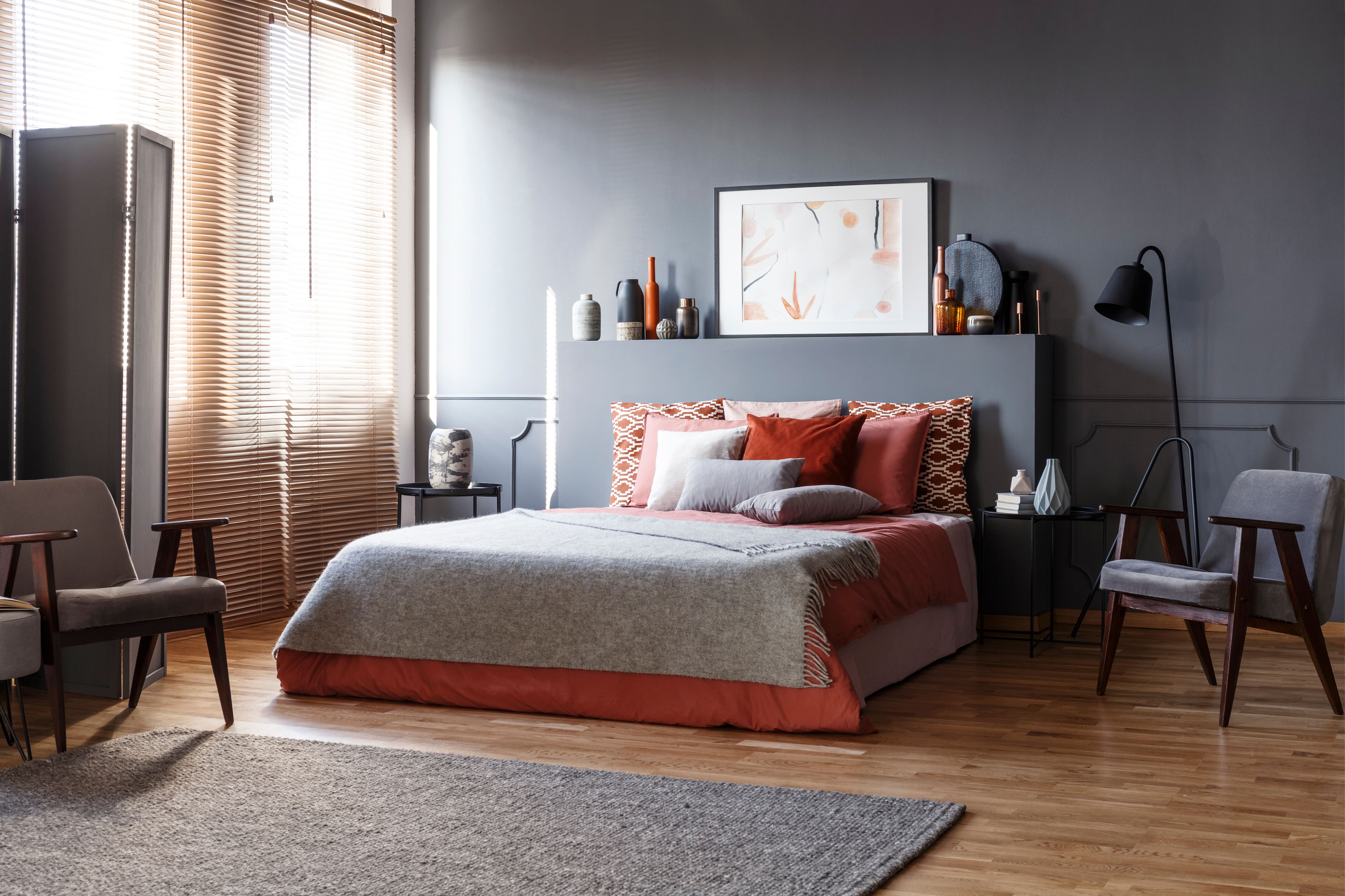 Modern gray bedroom with layered blankets, floor lamp, chair, and monochrome wainscoting