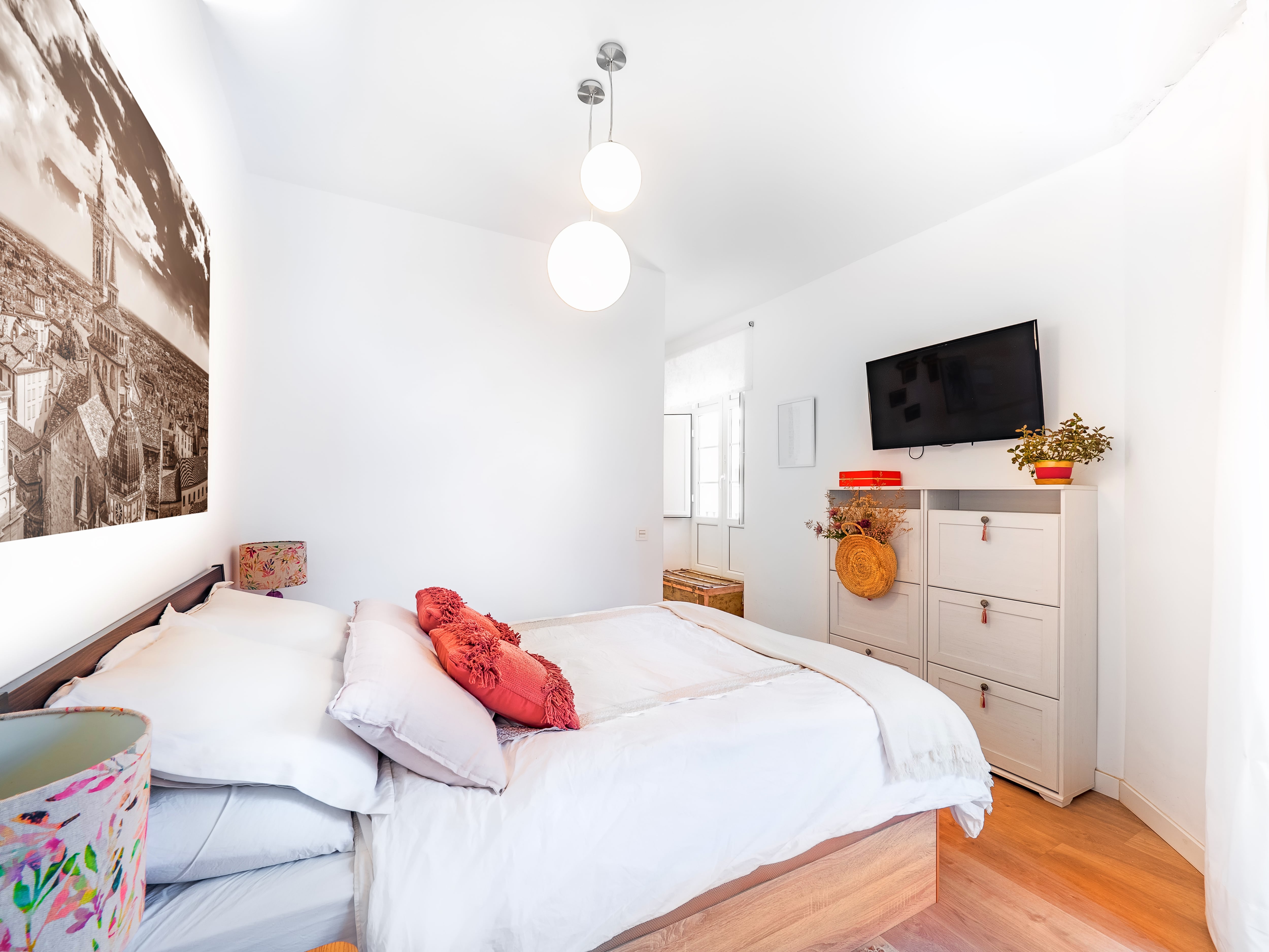 Bright, modern bedroom with wall-mounted TV, white dresser, and wooden bed