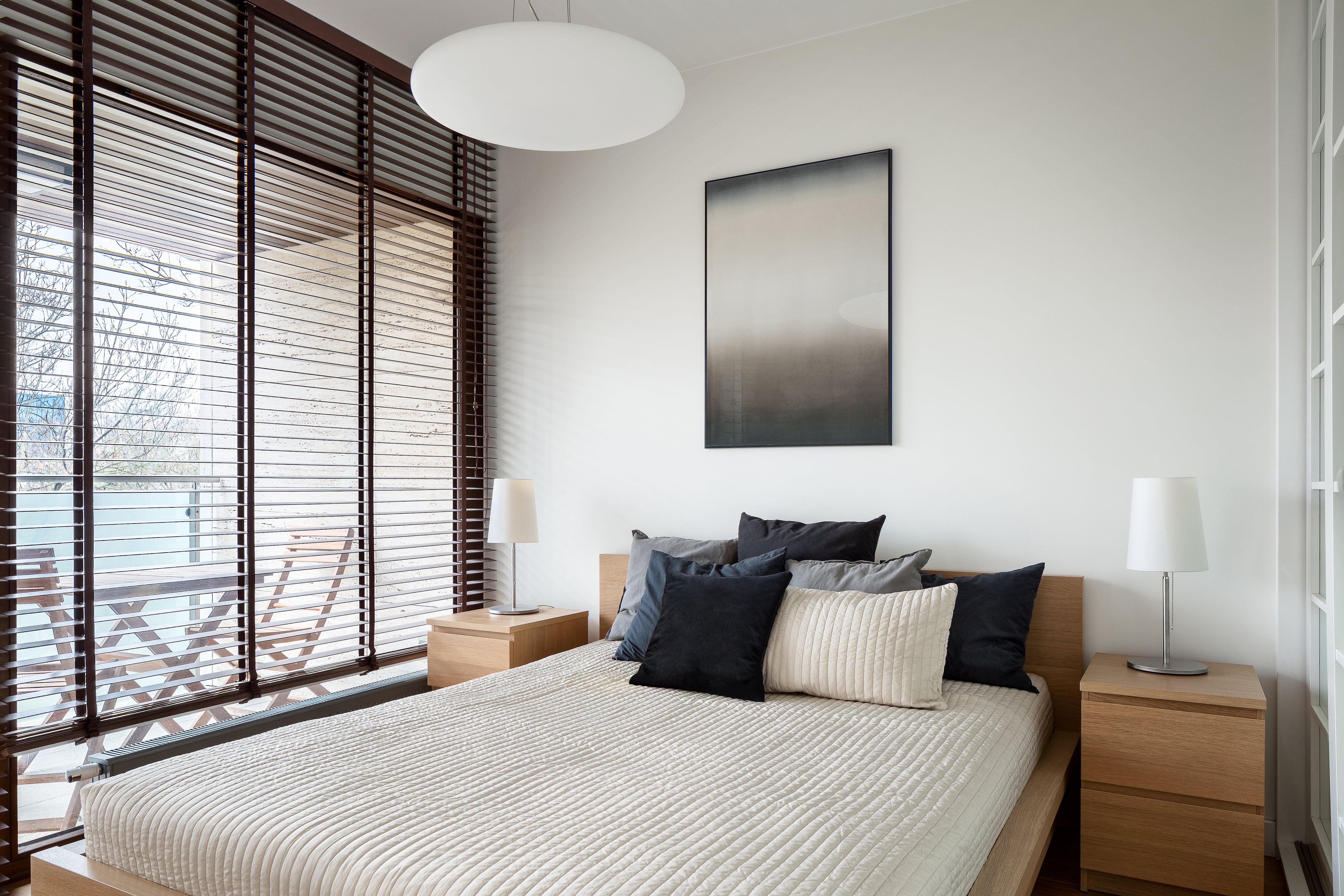 Small, cozy bedroom with floor-to-ceiling windows, wood blinds, two nightstands, and matching table lamps