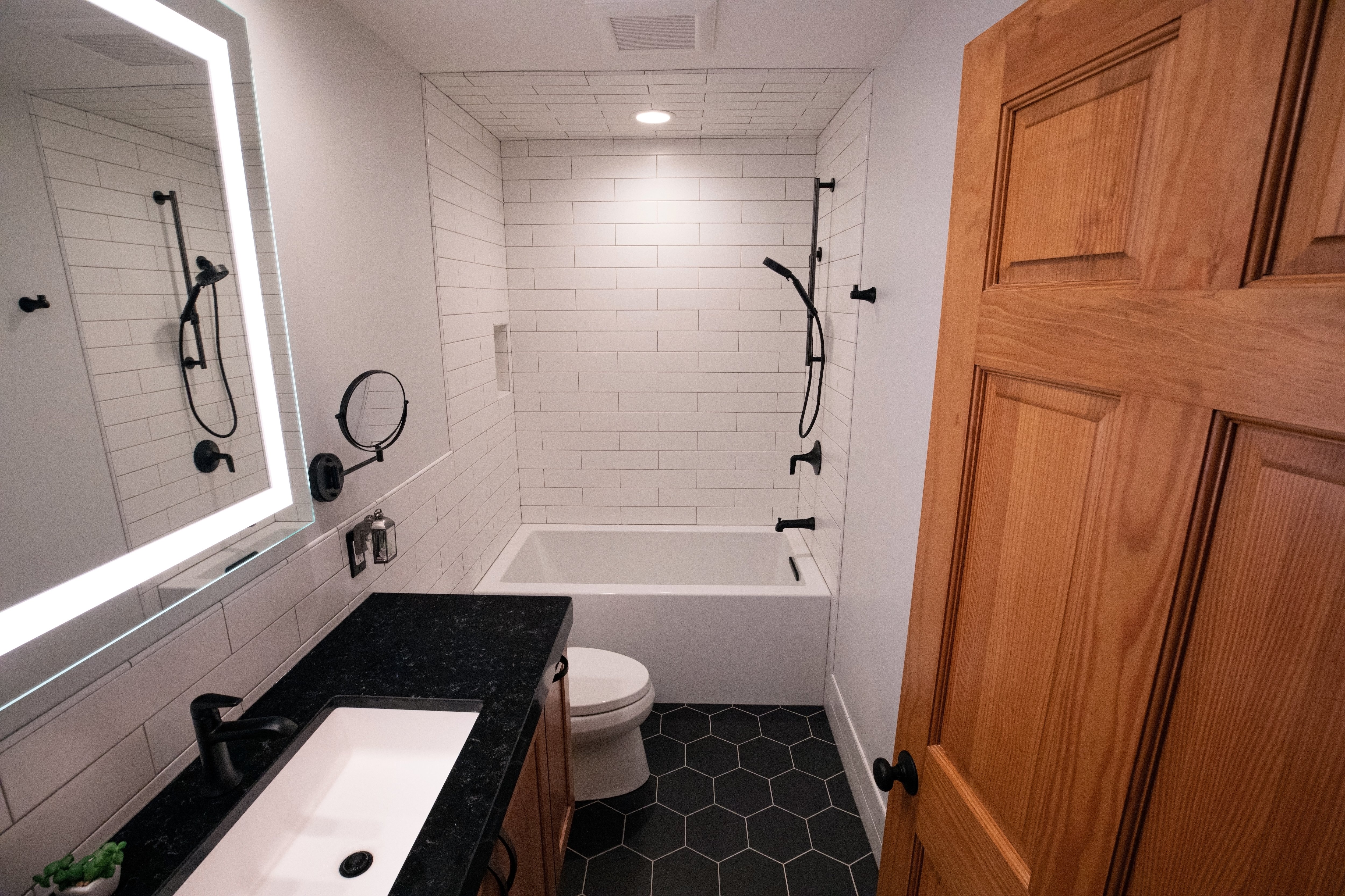 Bathroom with black honeycomb tile floor, black vanity, matte black fixtures, subway tile shower wall, and lighter mirror