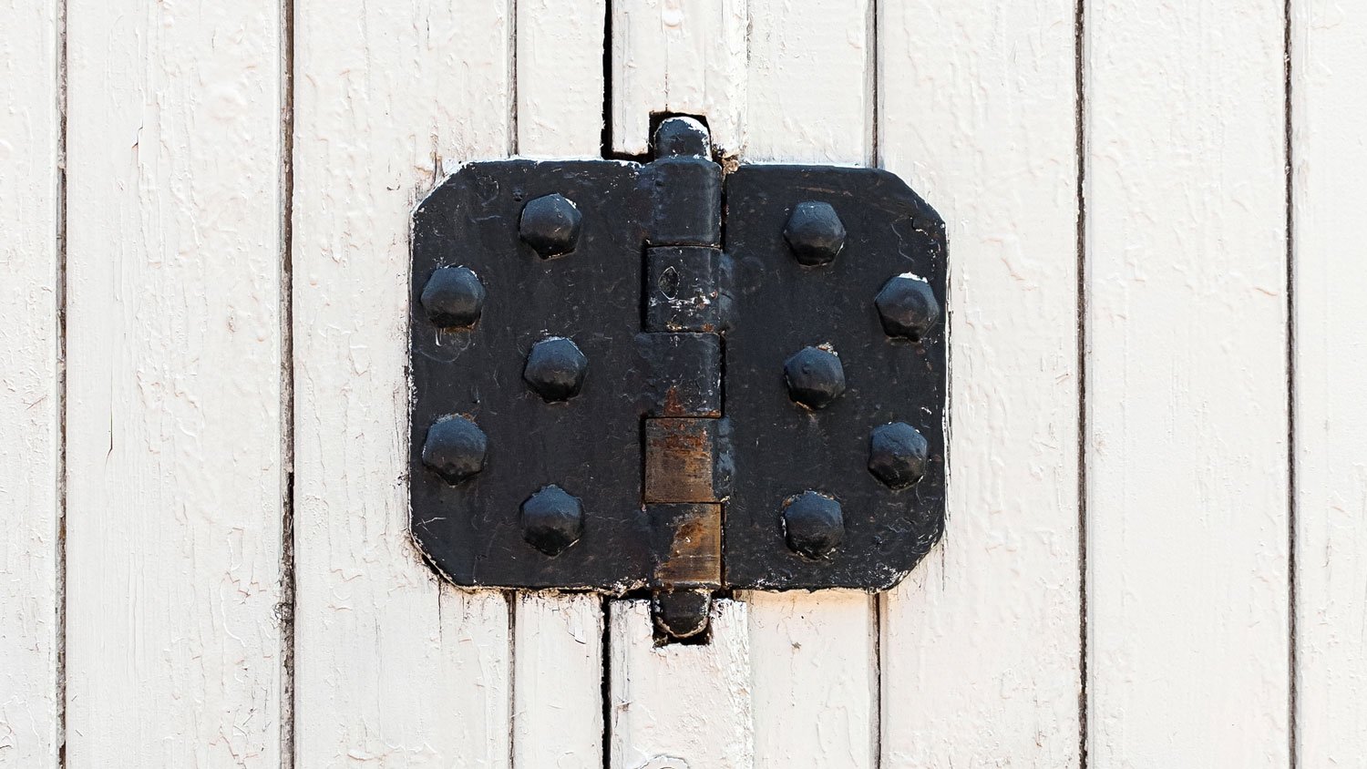 Vintage black door hinges on a white fence