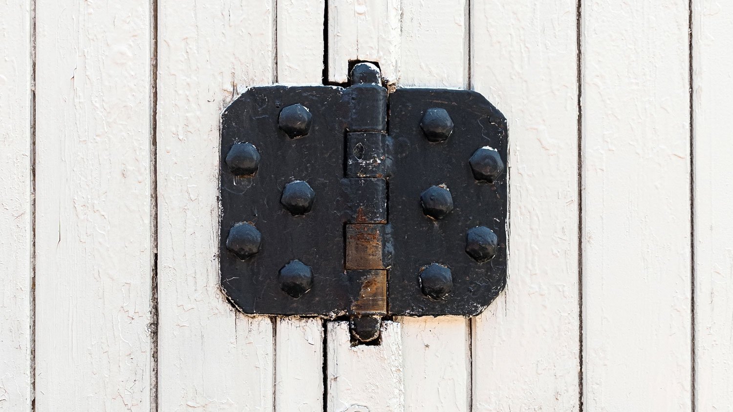 Vintage black door hinges on a white fence  