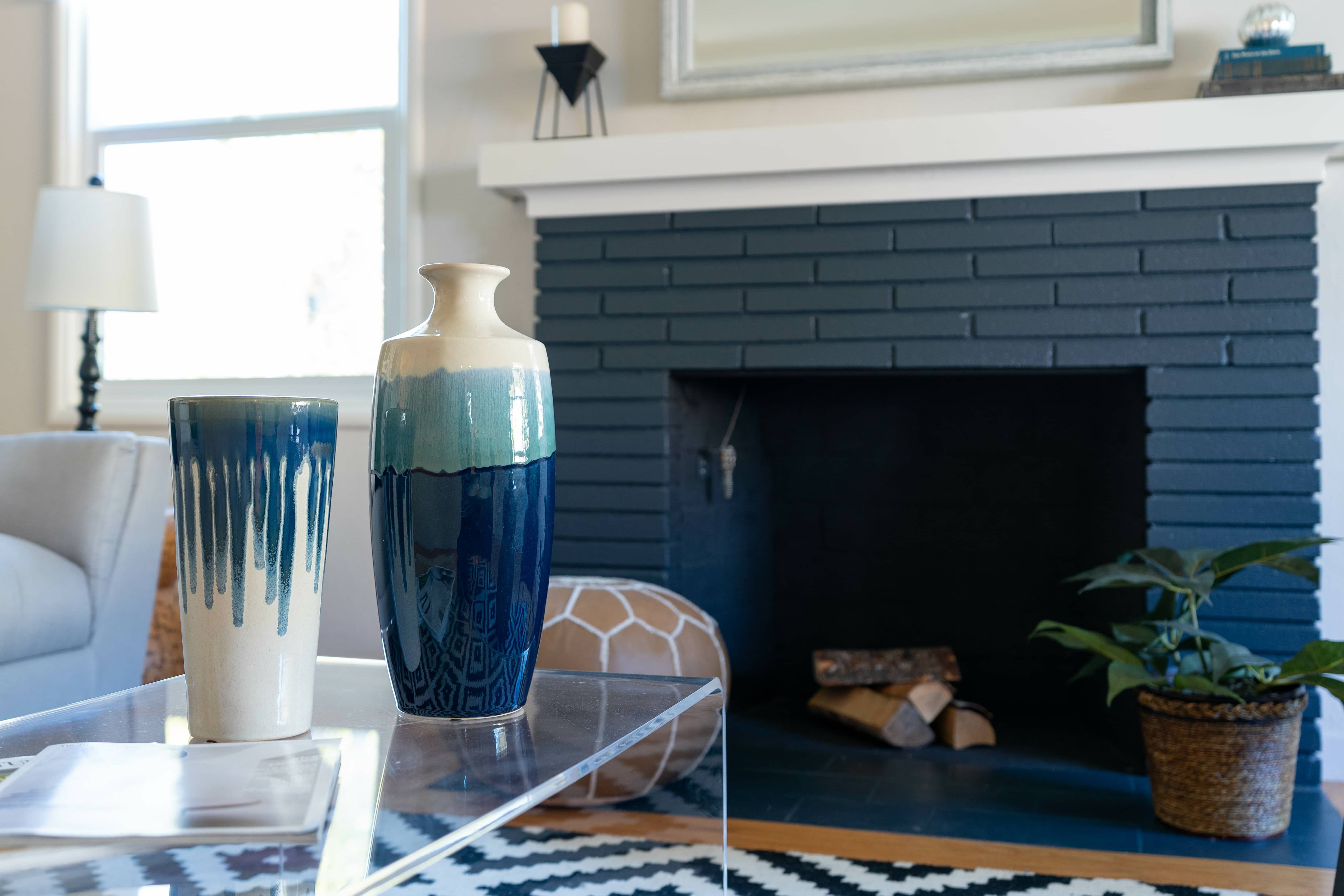 Navy painted brick fireplace with white mantel, acrylic coffee table, blue vases, leather ottoman, and black and white rug