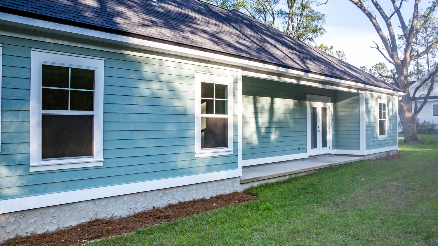 Rear view of a brand new construction house with blue siding, a ranch style home with a yard on a sunny day