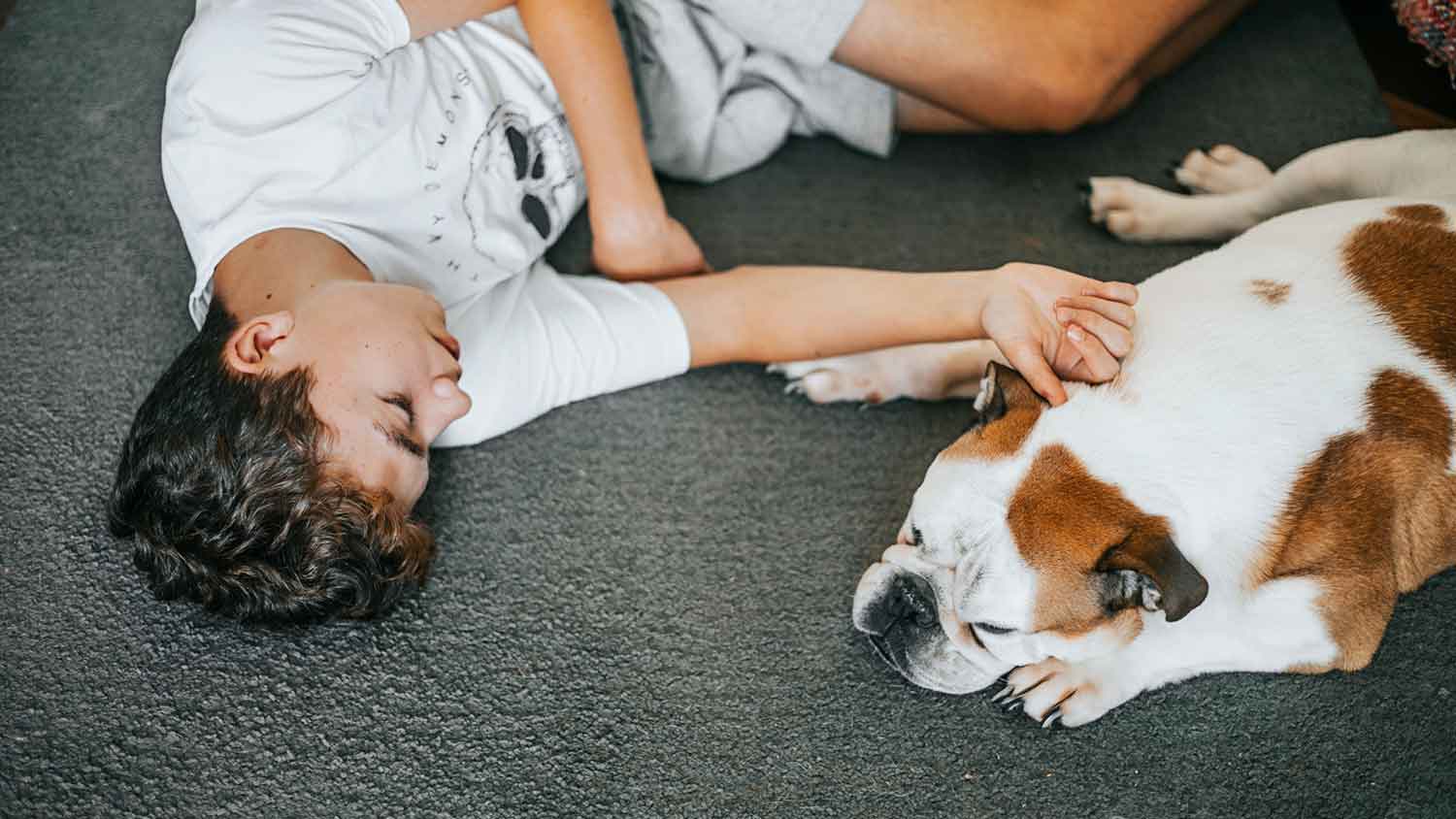 A teen boy and his dog are lying on the carpet