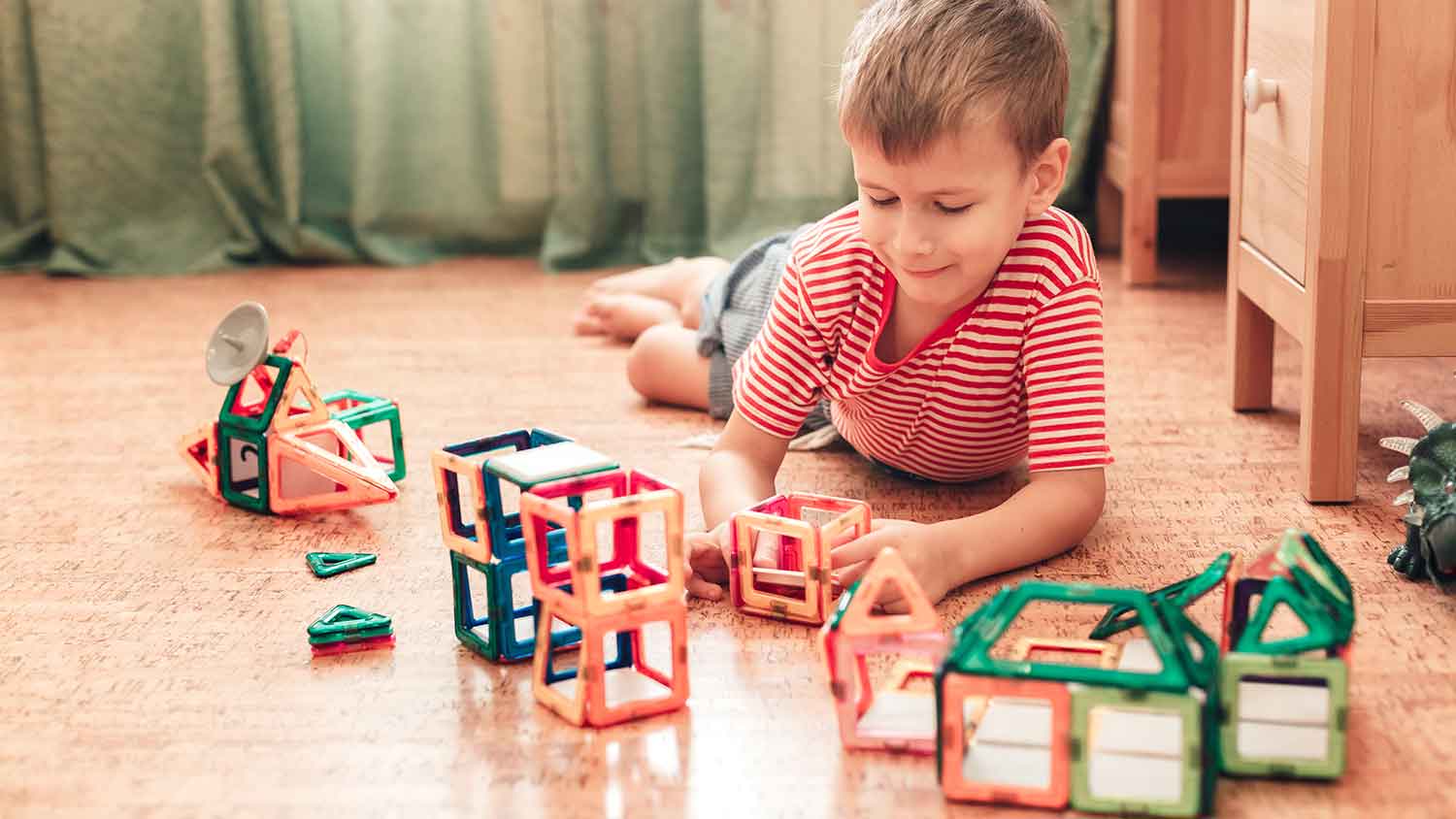 Boy sitting on a cork flooring playing with toys 