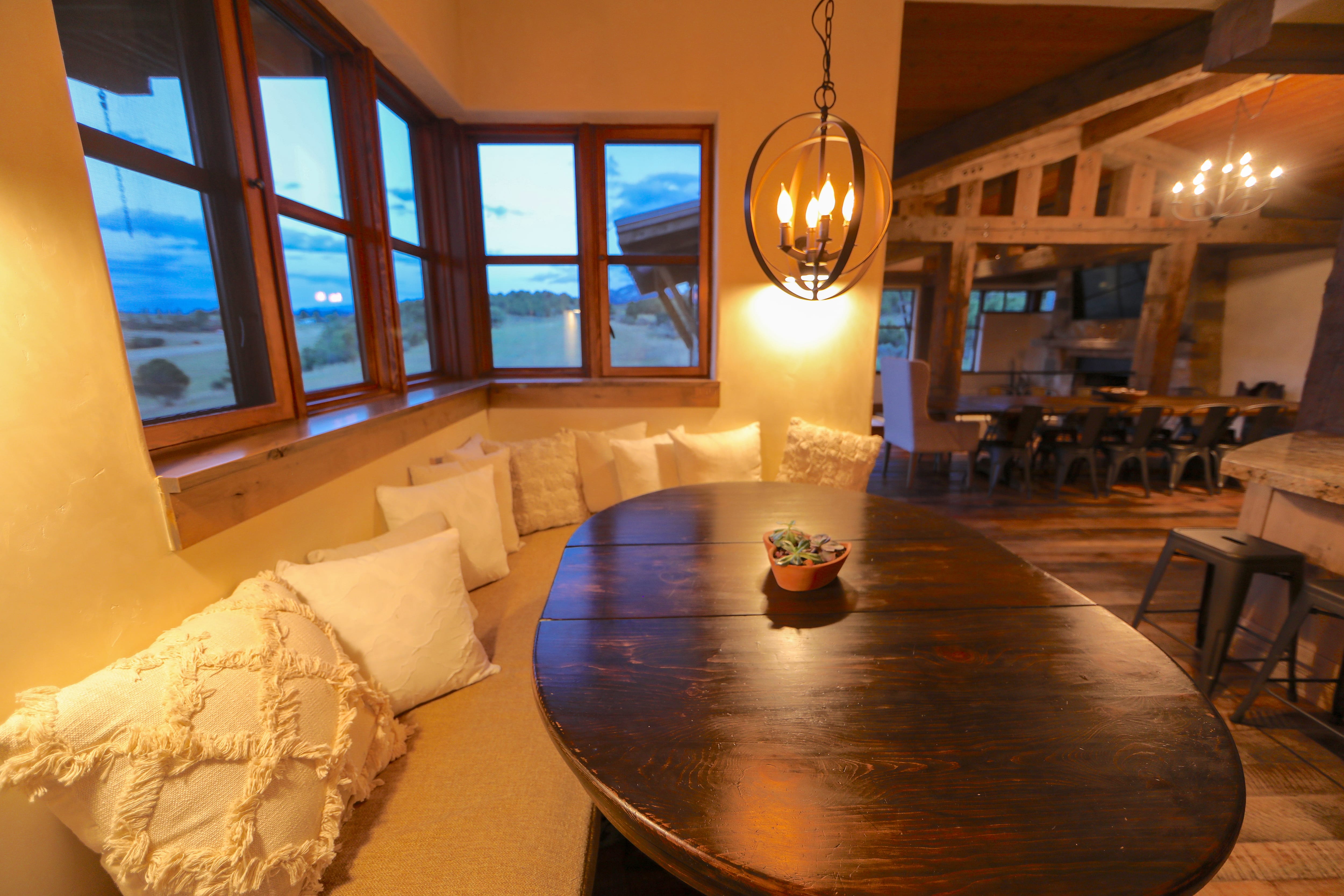 A large breakfast nook in dim lighting underneath a set of windows