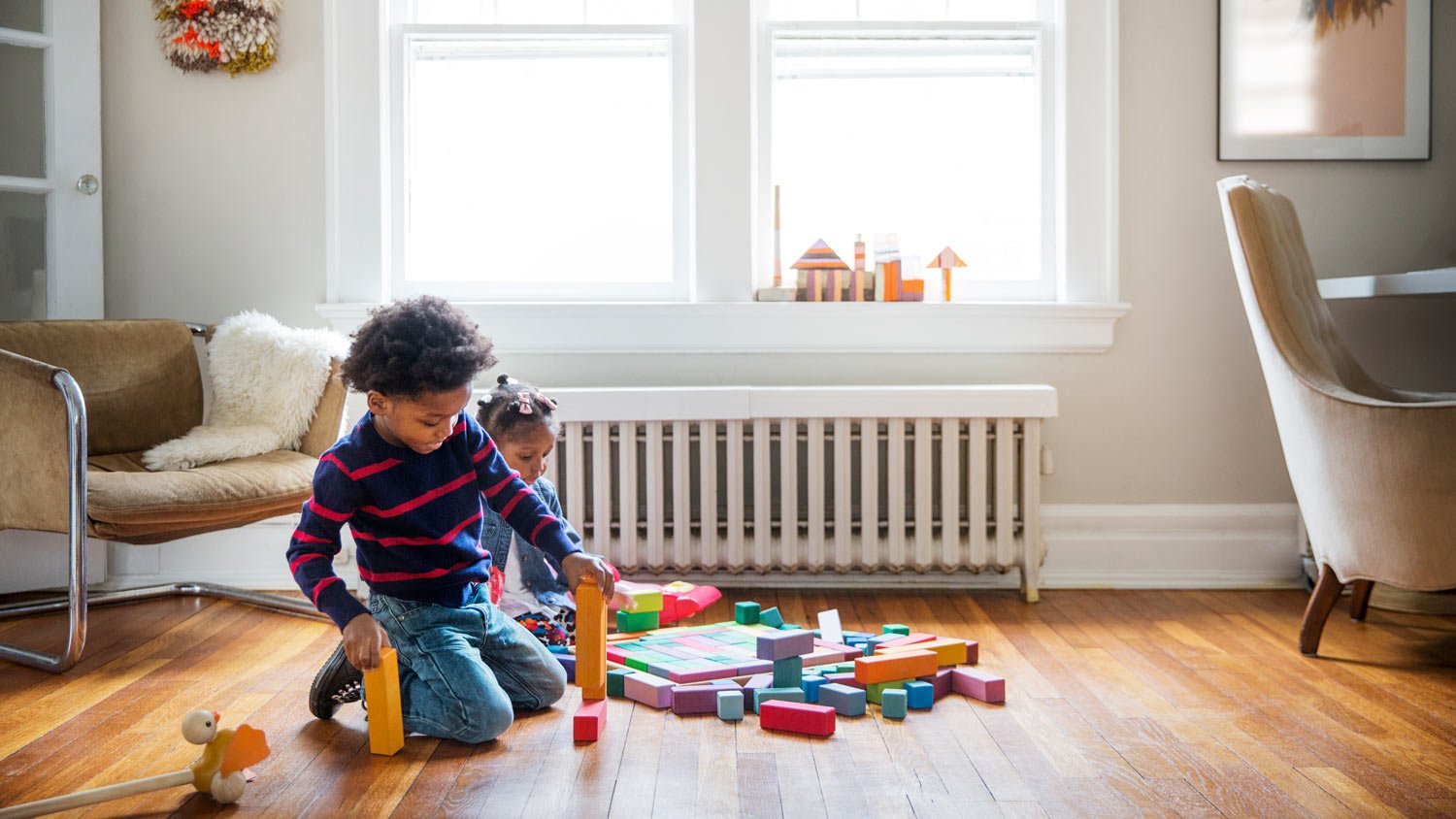 A sister and her brother playing with their toys on the floor