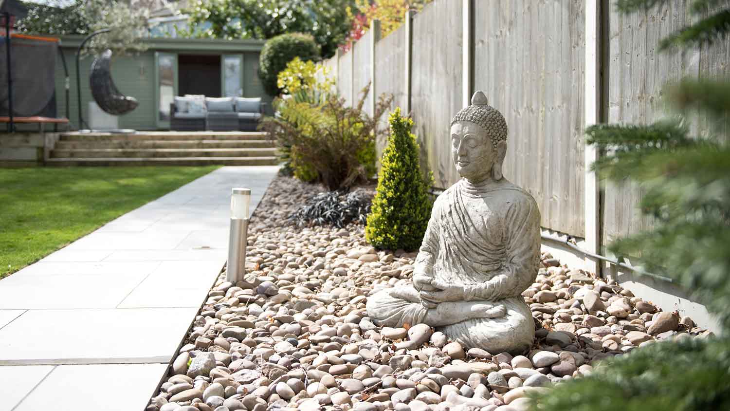 Budha garden sculpture sitting on a flower bed 