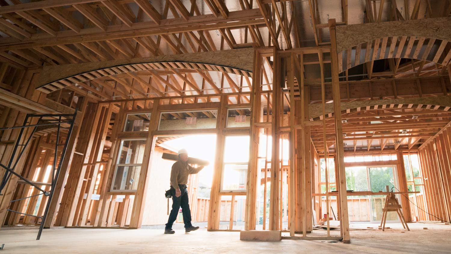 A builder walking with a plank of wood on a construction site