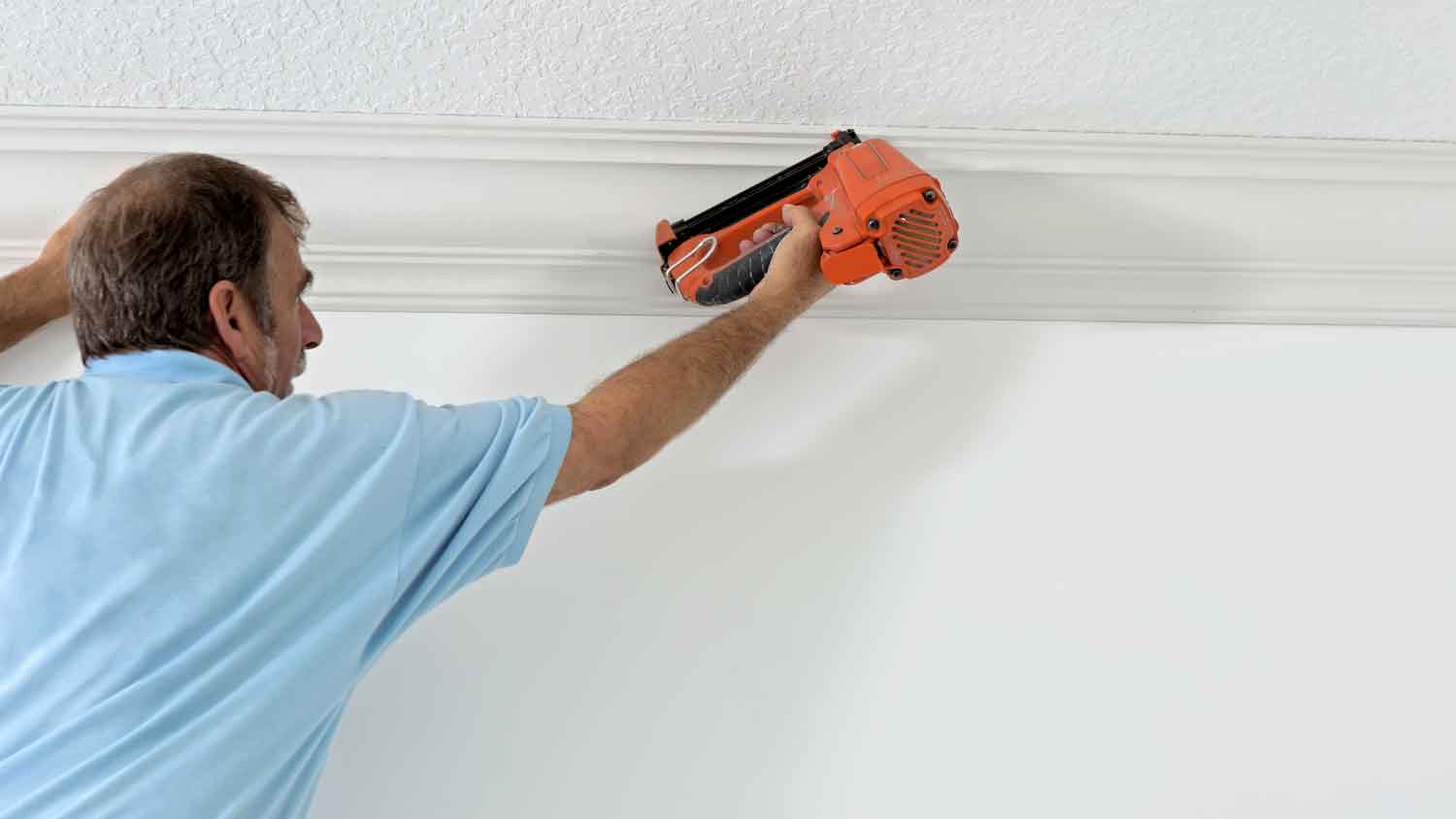 Carpenter using a nail gun to install crown molding