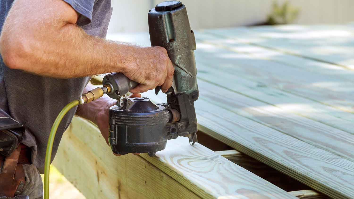 Carpenter using nail gun to install wooden deck 