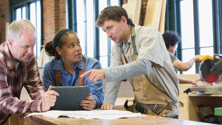 Carpenter using tablet in workshop with team members