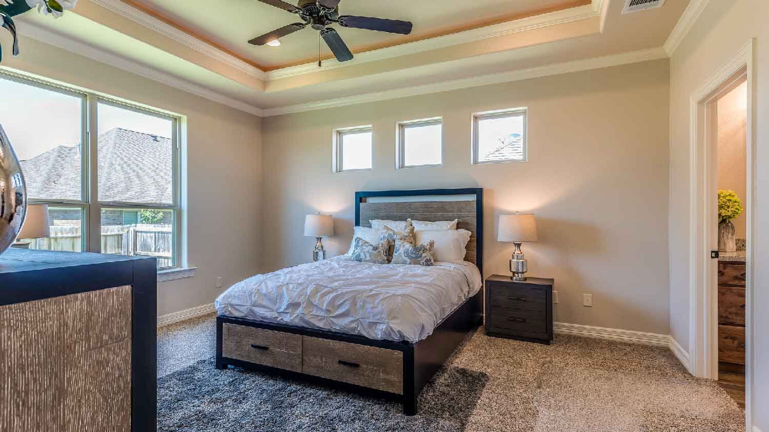 A carpeted bedroom with an area rug at the end of the bed