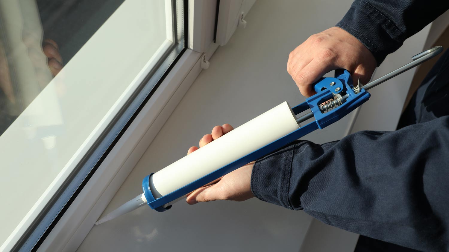 man sealing window with caulk