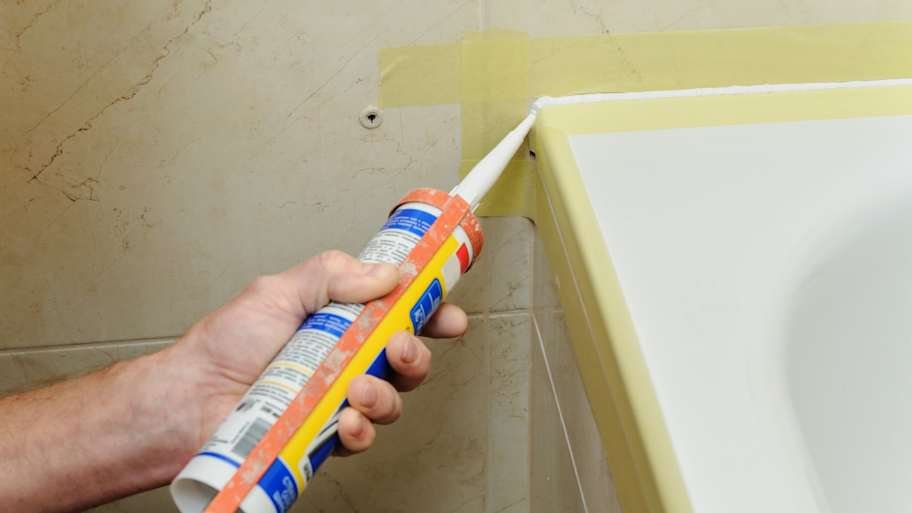 man caulking tile corners of bathtub