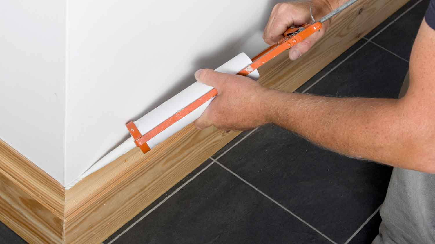 Worker using caulk to install wooden baseboard in the house