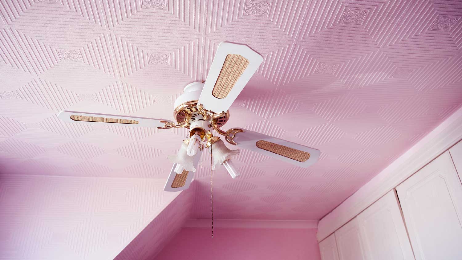 A ceiling fan with a light on a pink textured ceiling