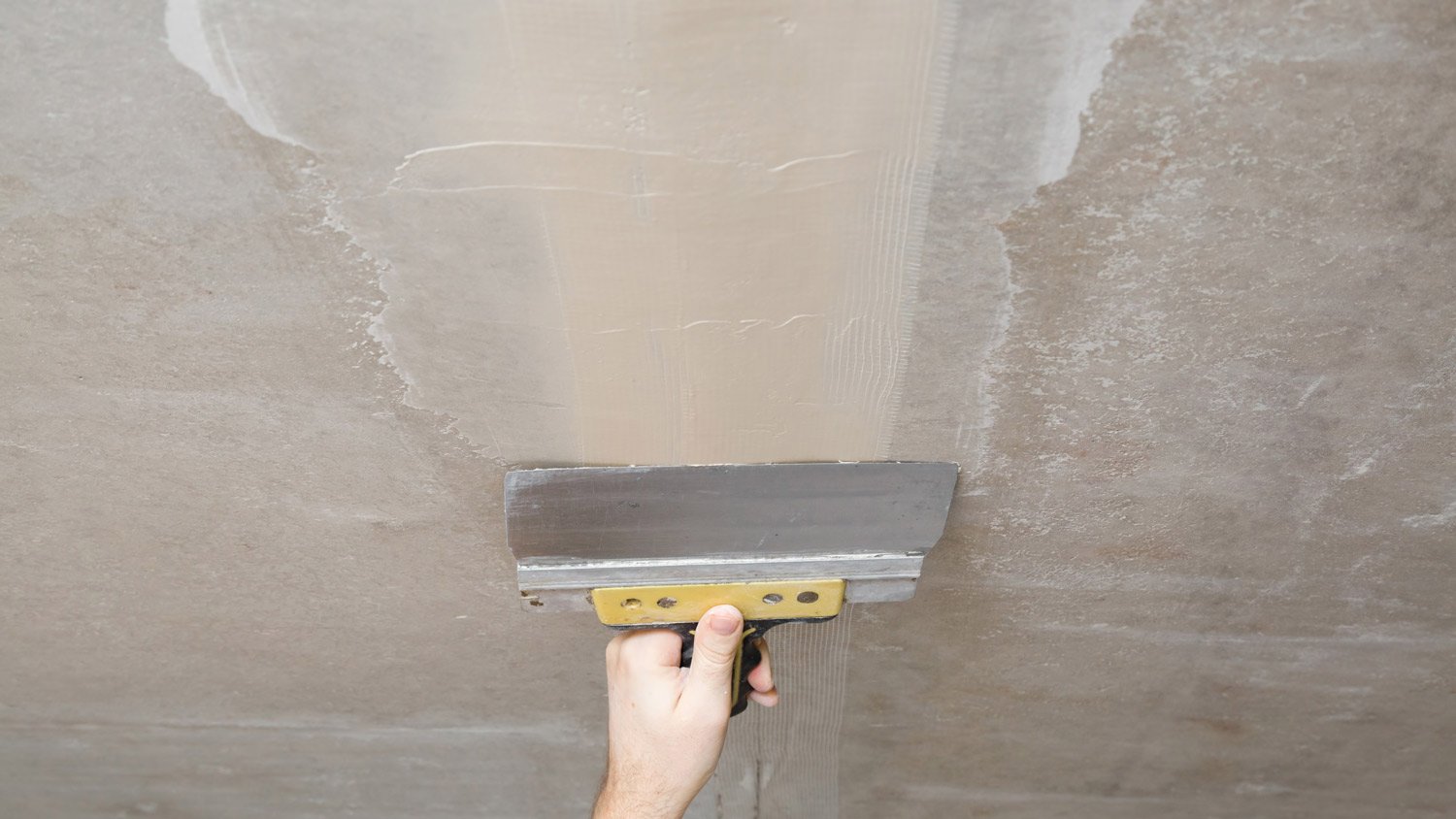 Young adult man hand using spatula and plastering ceiling with putty