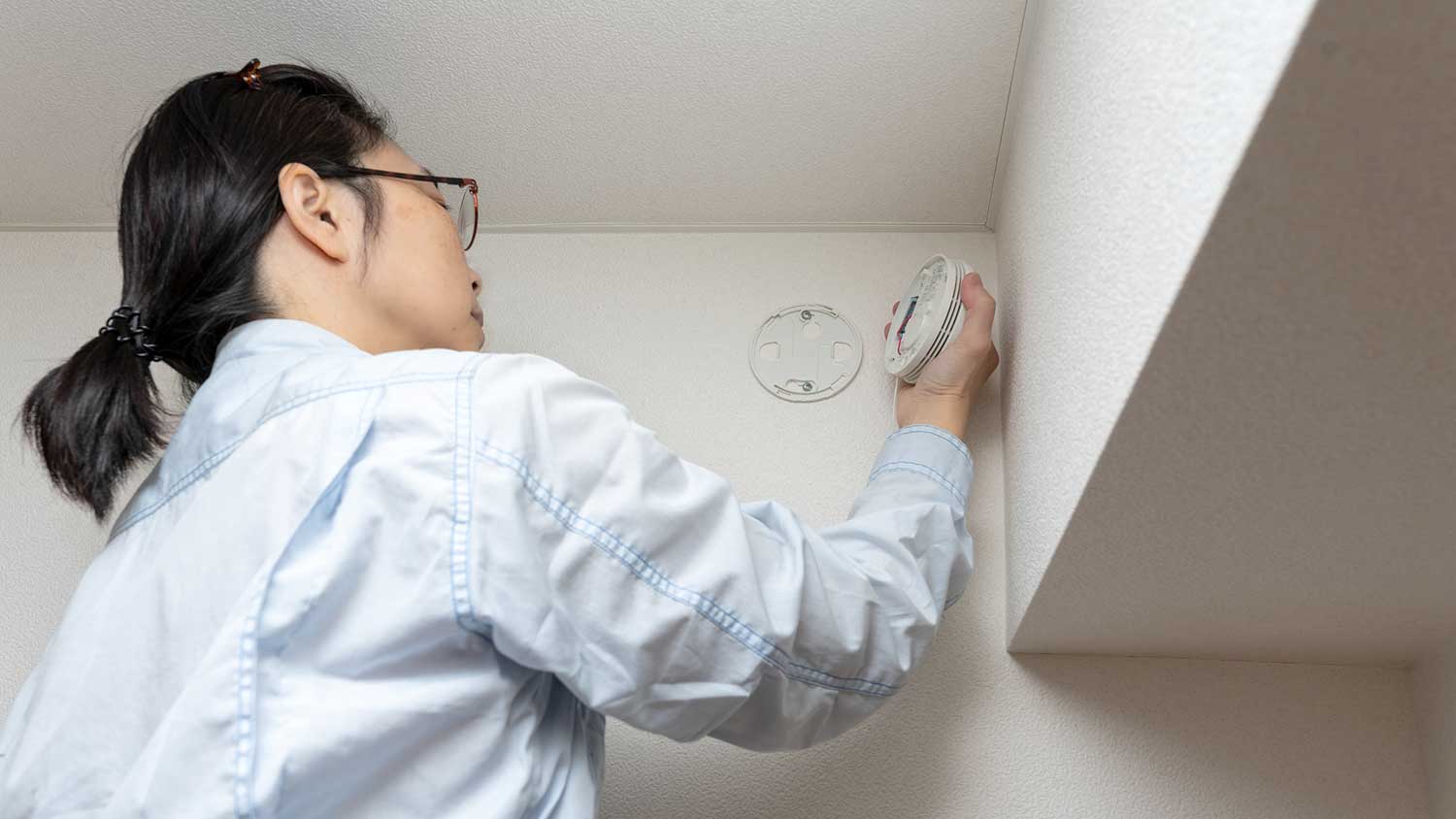 Woman checking smoke detector at home