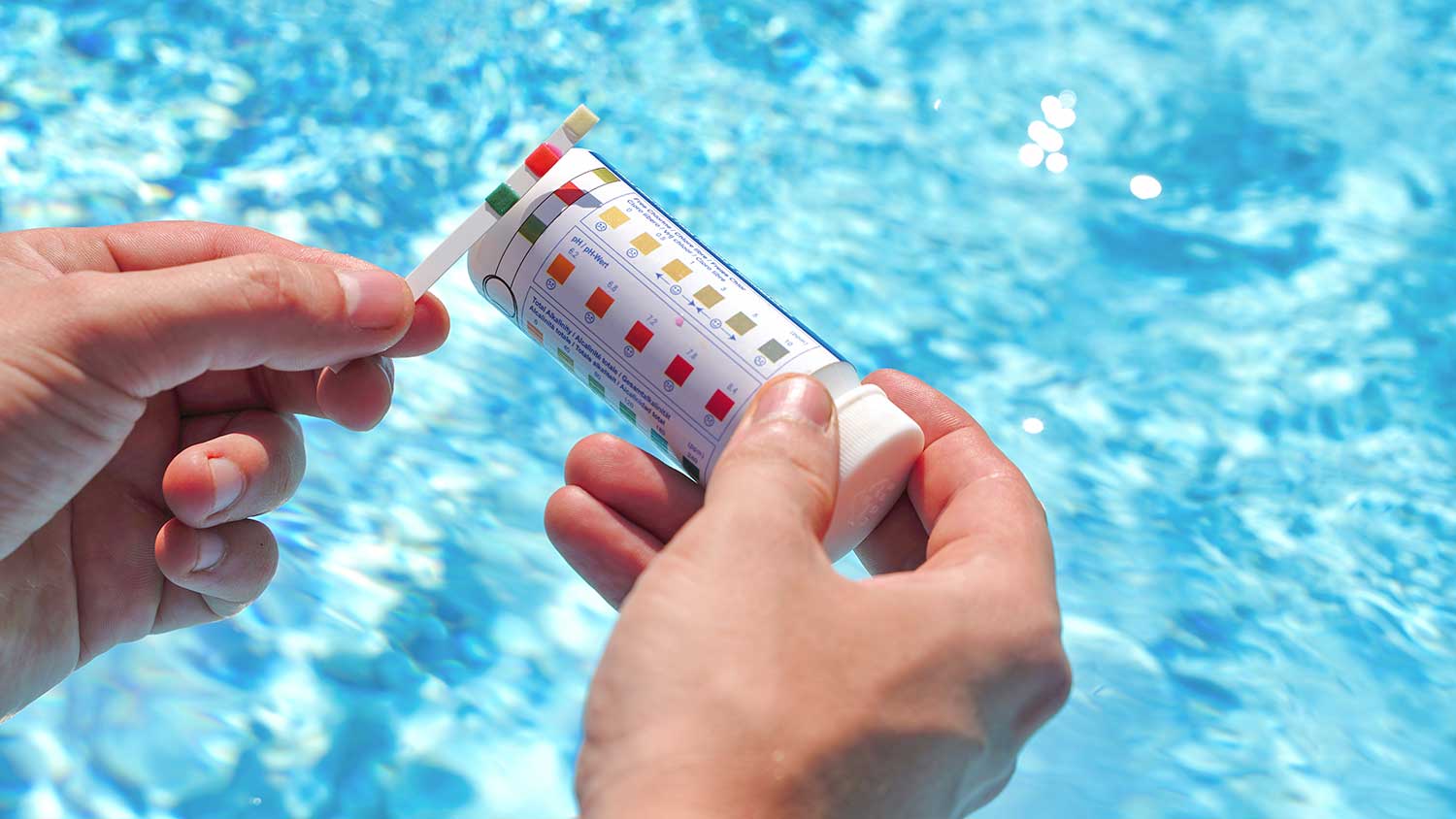 Hand holding swimming pool test strip checking water levels