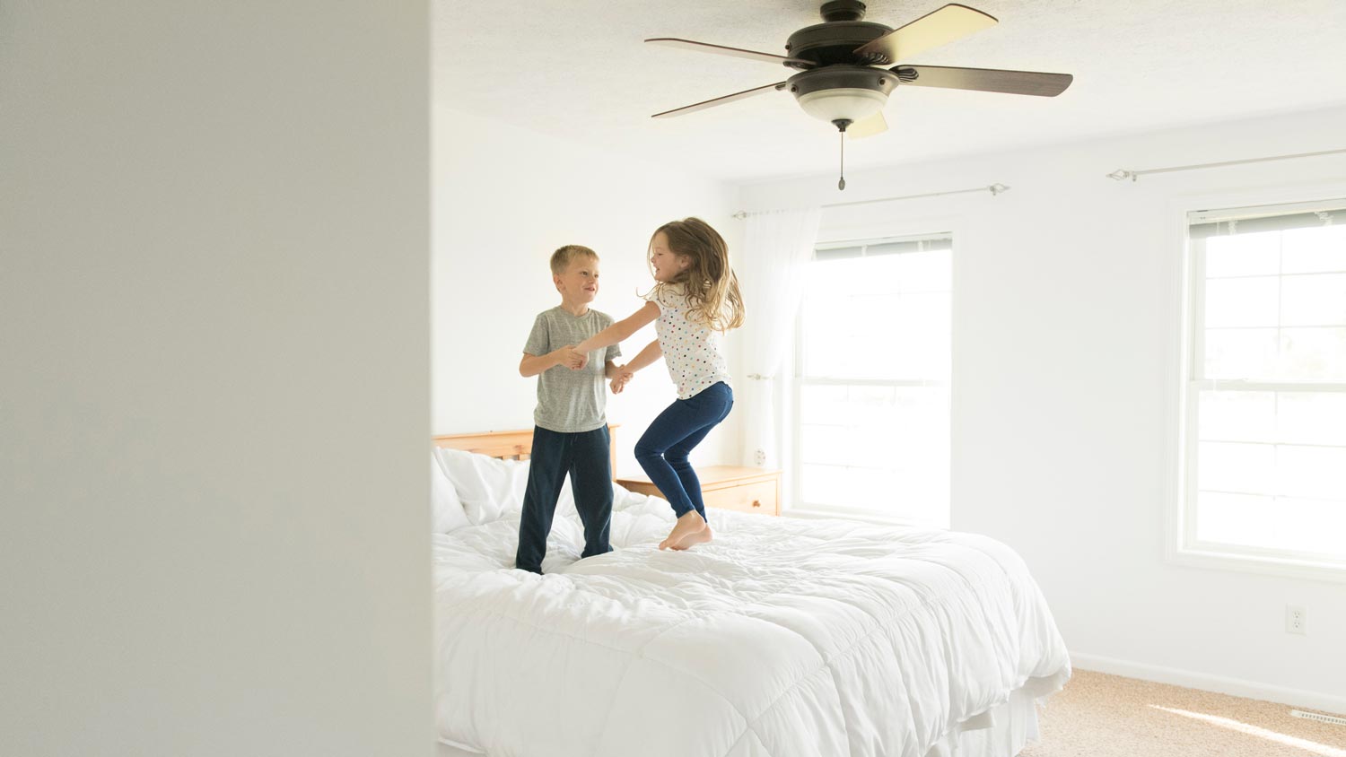 Children holding hands while jumping on bed