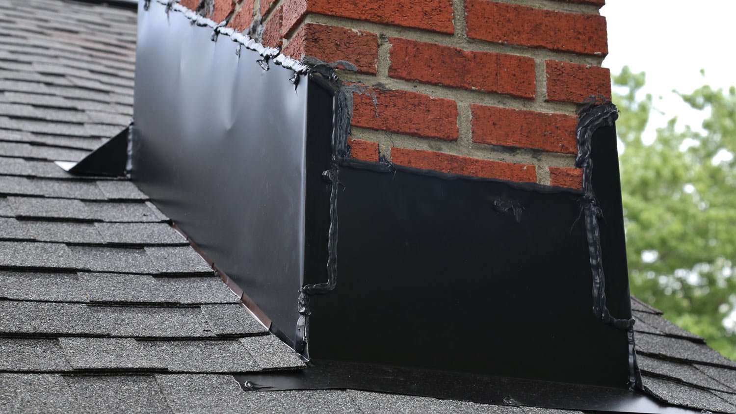 Metal flashing and caulk on a roof and brick chimney