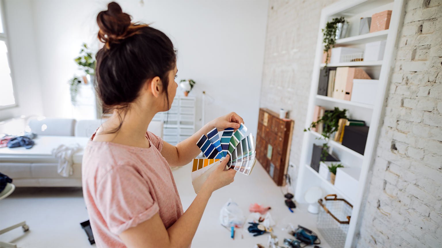 Young woman during reconstruction of apartment holding color chart and choosing the right color for the wall