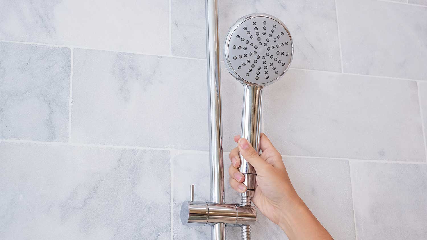Hand holding a showerhead installed in the shower