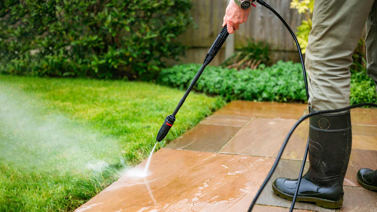 man cleaning patio tiles with pressure washer