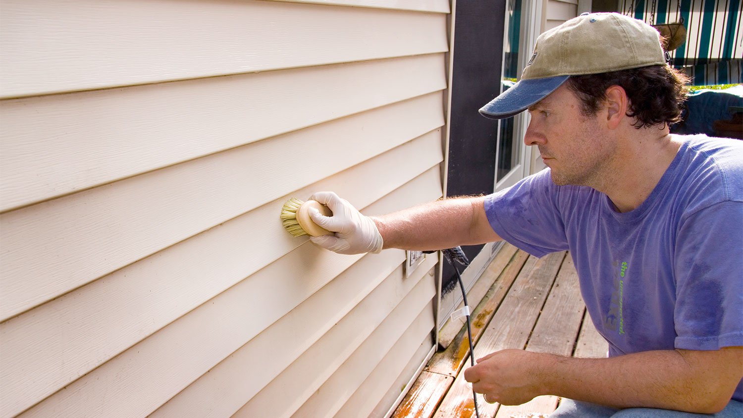 man washing vinyl siding of house with brush